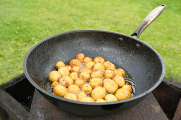 Baby potatoes fried in black metal pan in hot oil.