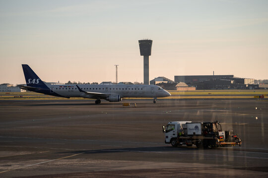 Kastrup, Denmark - 01-20-25: Cold winter evening at CPH Airport, Copenhagen, Kastrup lufthavn. SAS Embraer E195LR Taxiing with controll tower in background and airport vehicle in front.