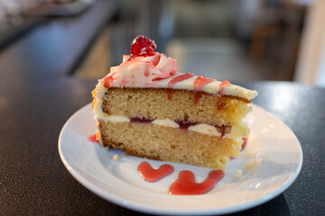 A slice of bakewell cake with a raspberry topping on a white plate. The cake is cut in half and has a drizzle of raspberry sauce on top