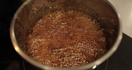 Close-up of a metal pan on a professional pastry hob. Melting butter, boiling caramel and mixing...
