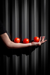 Conceptual Minimalist Photography: Three Red Tomatoes Balancing on an Outstretched Arm Against a Dark Metal Background