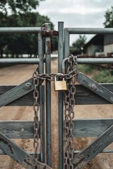 Locked gate securing entrance to farm road surrounded by greenery on a cloudy day