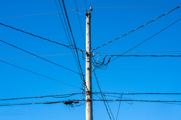 Wooden telephone and power line utility pole against a sunny blue winter sky, lots of lines and cables running in all directions
