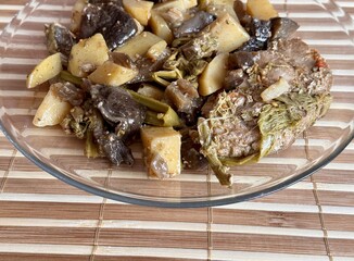 The hot dish includes baked potatoes, eggplant, mushrooms, Far Eastern bracken with paprika and spices. Delicious food on a glass plate on a bamboo tablecloth in a restaurant
