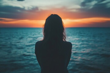 Fototapeta premium Silhouette of a woman sitting near the ocean during sunset