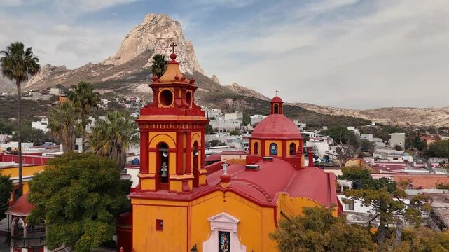 Colourful parish with Pe&ntilde;a de Bernal in the background in Mexico. Drone approaches the church and slowly rises, revealing the rock