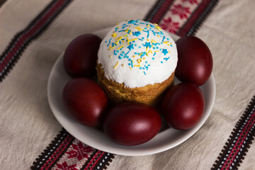 Traditional Easter bread sprinkled with yellow and blue sprinkles and krasanky (painted eggs) on a background with Ukrainian ornaments