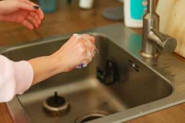 a girl washes the kitchen sink and pours cleaning agent onto a sponge