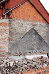 Urban demolition site with exposed brick walls, rubble piles, and construction equipment. City buildings in the background highlight redevelopment or construction themes in an urban setting.