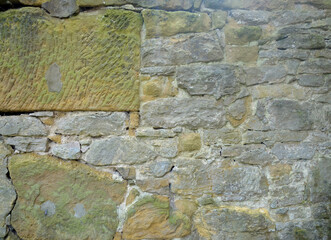 The image is a close-up of a stone wall. The wall is made up of small, irregularly shaped stones of...