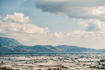 Greenhouses stretch across the valley beneath a cloudy sky. Agricultural fields thrive in a rural...