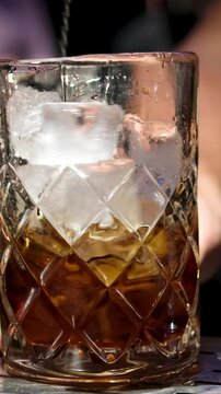 Close up of a professional bartender is mixing an alcoholic cocktail with professional crystal long lasting ice cubes to customers at the bar or disco club. Professional bartender masterly creating
