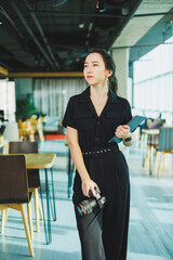 A Chic Young Woman Dressed in a Stylish Outfit Poses with a Camera in a Modern Workspace