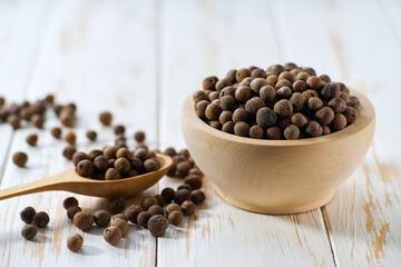 wooden bowl with allspice or Jamaican pepper seeds on a white wooden table, selective focus.