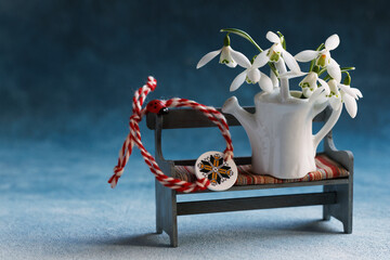 Card for the holiday of March 1, Martisor, Baba Marta. Decorative bench with a watering can, a bouquet of snowdrops, red and white  bracelet Martenitsa, copy space, festal