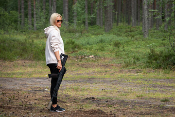 Blonde girl in sunglasses with a rifle with a silencer in her hand in the forest in nature.