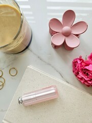 Elegant flat lay of pink roses, rings, flower hair clip, and beauty products on a marble surface.