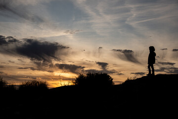 boy backlit at the top of a small hill at dusk. not recognizable. silhouette.