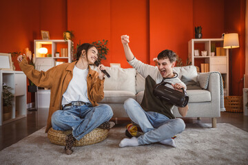 Naklejka premium young couple girlfriend and boyfriend sit on floor and sing karaoke