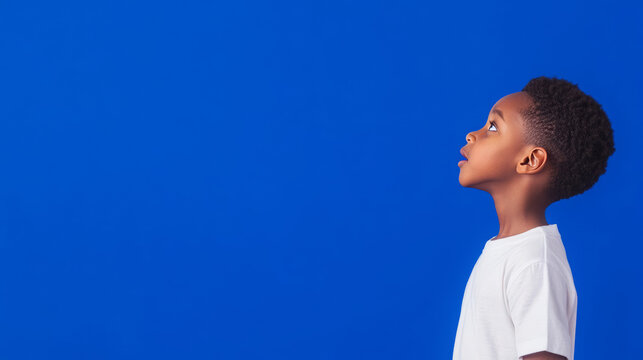 young boy gazes upward against vibrant blue background, filled with wonder