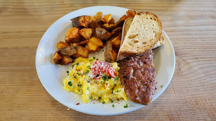 American Western breakfast with crispy homemade sausage, scrambled eggs, hash browns and sour dough toast on a plate