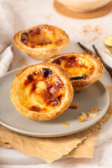 Three Pastel de Nata, Portuguese custard tarts, are presented on a plate with cinnamon and vanilla beans.