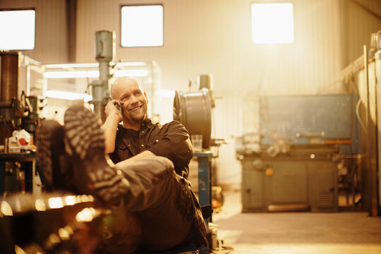 Middle aged caucasian man mechanic talking on his smart phone while working in a mechanics shop