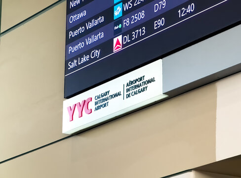 Calgary, Alberta, Canada. Feb 14, 2025. A close-up of a YYC Calgary International Airport sign with a digital flight information display showing destinations like Ottawa and Salt Lake City.