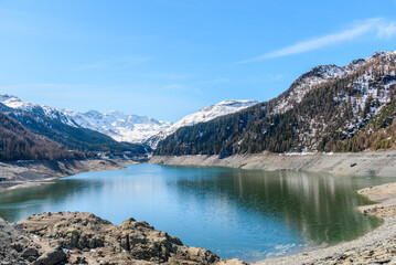 View of a reservoir overlooked by snowy peaks in the Swiss Alps on a clear early spring day