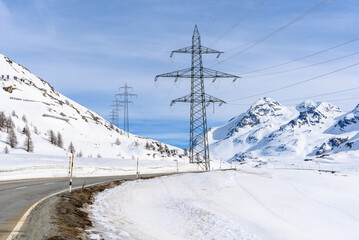 High voltage lines over a curvy mountain road in a snowy mountain landscape on a partly cloudy day