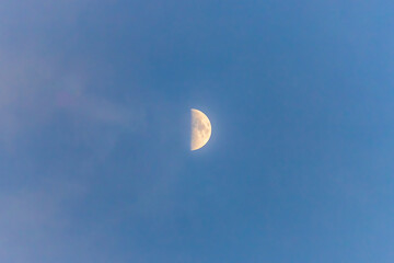 Half moon during daytime in sky, blue sky and clouds in background