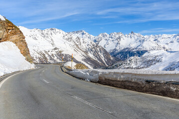 Empty stretch of a curvy road through a majestic snowy mountain landscape in Switzerland on a clear day