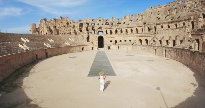 Woman in summer attire walking through historical colosseum amphitheater in El Jem, Tunisia