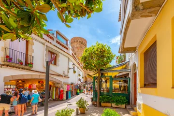 The narrow streets of shops and sidewalk cafes in the whitewashed old town of Tossa de Mar Spain, Costa Brava, with the 12th century castle tower in view. 
