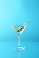 Martini cocktail with olives in glass on light blue background