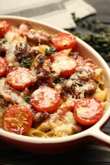 Delicious pasta casserole with cheese, tomatoes, minced meat and thyme in baking dish on table, closeup