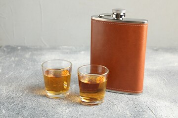 Hip flask and glasses with whiskey on grey table