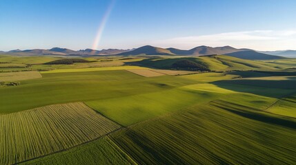 Obraz premium Aerial view of vibrant green agricultural fields and distant mountains with a rainbow.