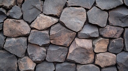 Fototapeta premium A textured wall made of irregularly shaped dark stones, showcasing natural tones and variations in color and texture.