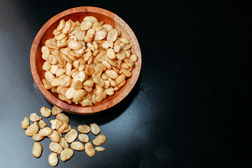 salted broad beans close-up in a wooden bowl. top view, good for recipe or commercial, isolated on black background