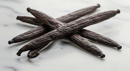 A few dark, wrinkled vanilla beans placed on a white marble background.