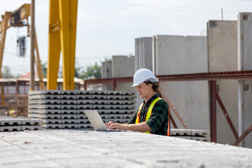Fototapeta premium Civil engineer in safety suit is using his computer or laptop to check the quality of slabs and precast floorboard in production line. A male engineer with his computer using technology in a factory.