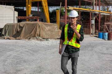 Civil engineer in safety suit is using his computer or laptop to check the quality of slabs and precast floorboard in production line. Male engineer using walkie talkie to communicate in a factory.