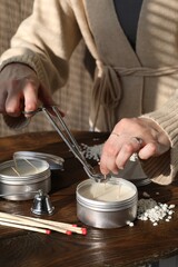Woman cutting soy candle wick with trimmer at wooden table, closeup