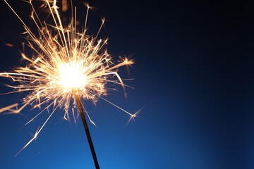 Bright burning sparkler on dark blue background, closeup. Space for text