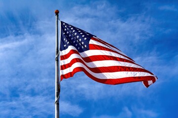 Fototapeta premium American Flag Waving Against a Clear Blue Sky a Patriotic Symbol that can be used for a poster or in graphic design