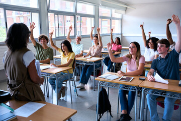 Happy group of multi-ethnic students sitting in classroom with their hands raised. Young smiling multiracial teenagers people answering the teacher question in class. Generation z high school concept