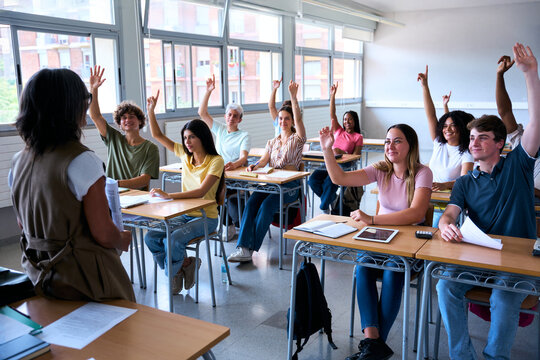 Happy group of multi-ethnic students sitting in classroom with their hands raised. Young smiling multiracial teenagers people answering the teacher question in class. Generation z high school concept