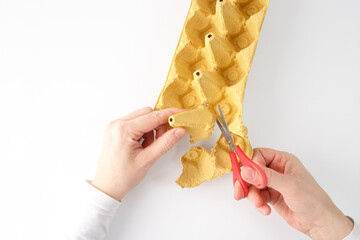 A pair of hands using red-handled scissors to cut a yellow egg carton. DIY project, activity for...