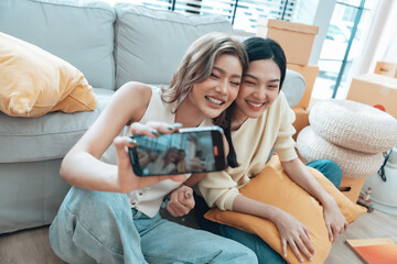 Two young Asian women smiling and happy while taking a selfie in their living room at home, looking at the camera